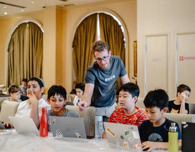 A Strive teacher helping a room of kids working on laptops