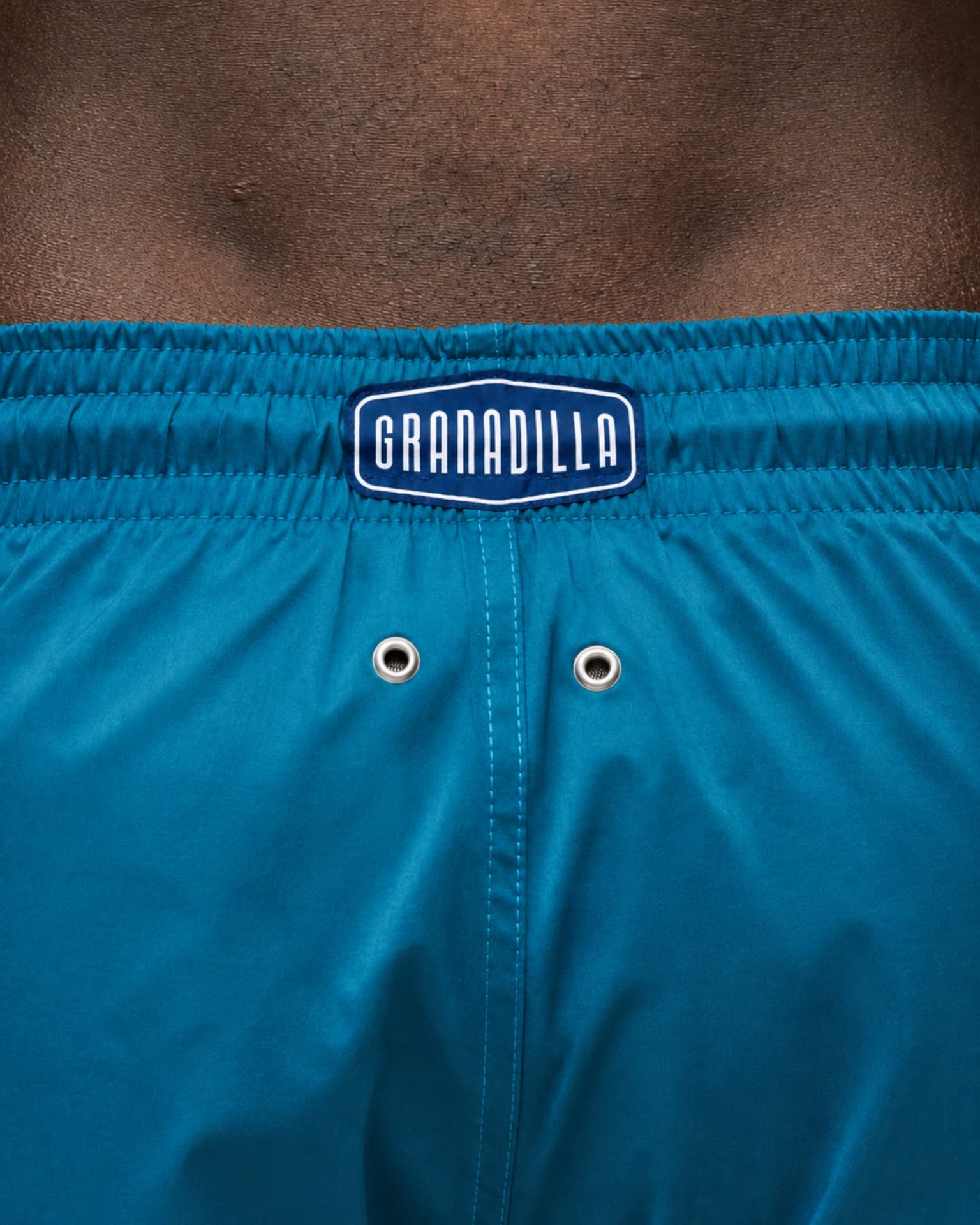 Granadilla logo patch on the waistband of teal swim shorts