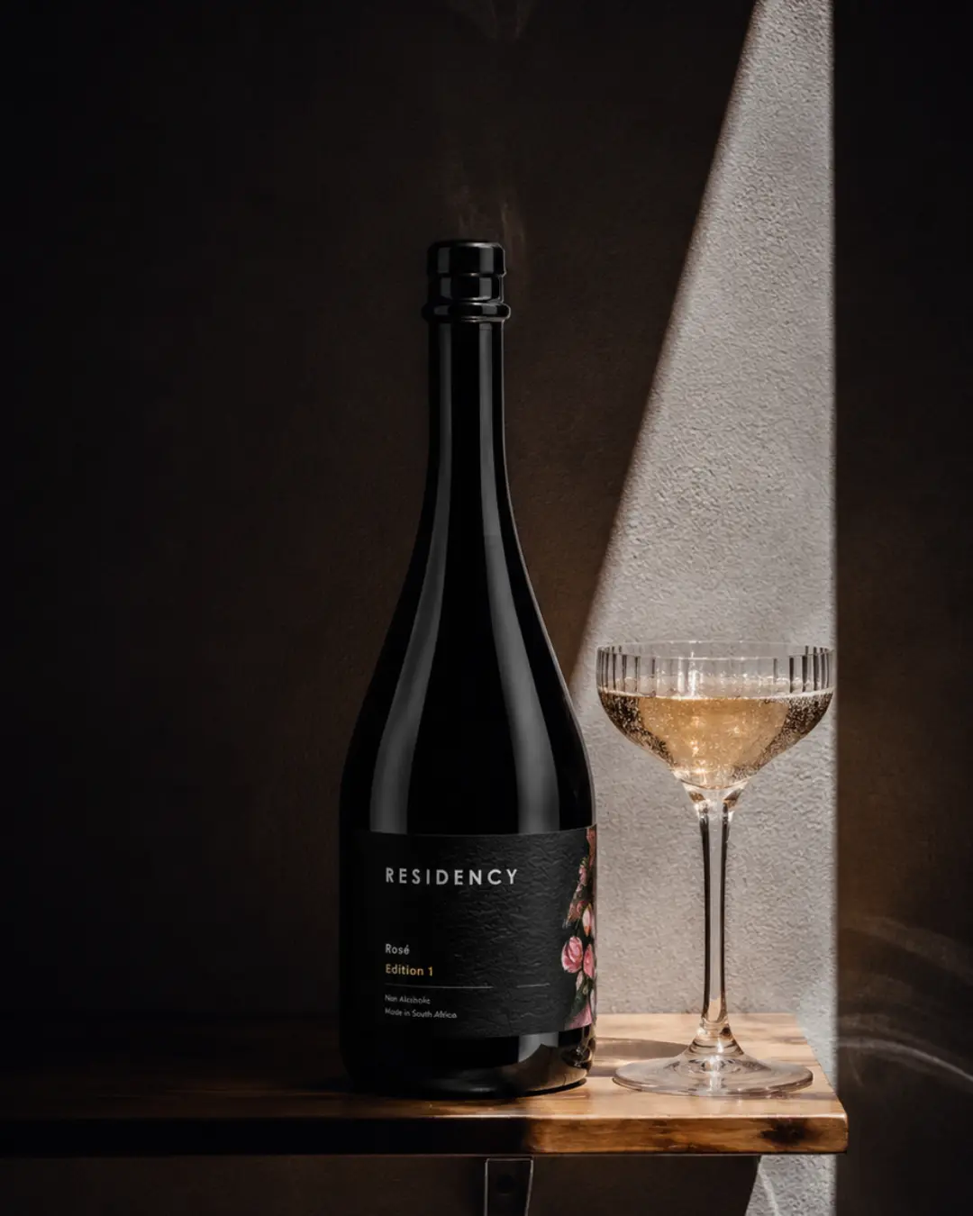 Residency Rosé Edition 1 bottle beside a filled coupe in a shaft of hard light