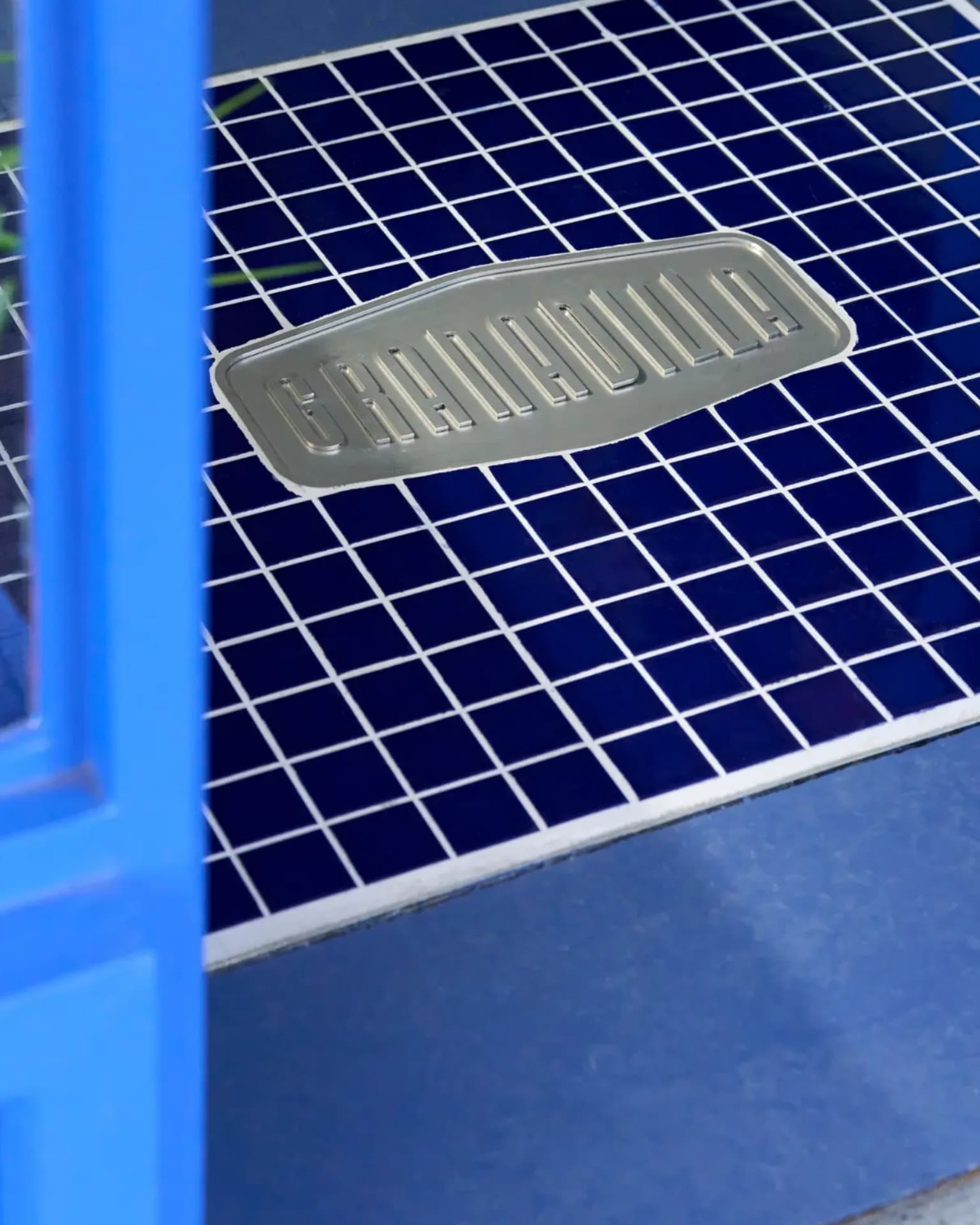 Brushed metal Granadilla plaque set into cobalt tiling at the store entrance