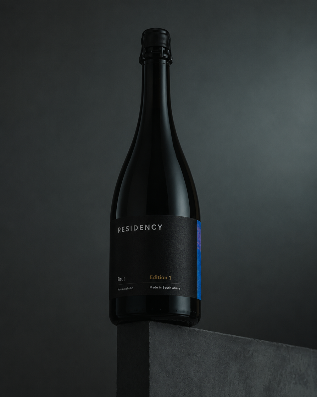 Residency Brut Edition 1 bottle balanced on a concrete edge against a dark backdrop