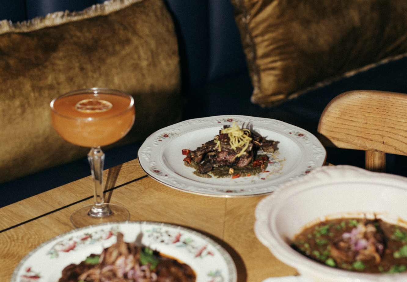 Plated dishes and a cocktail on a table inside Mother In Law
